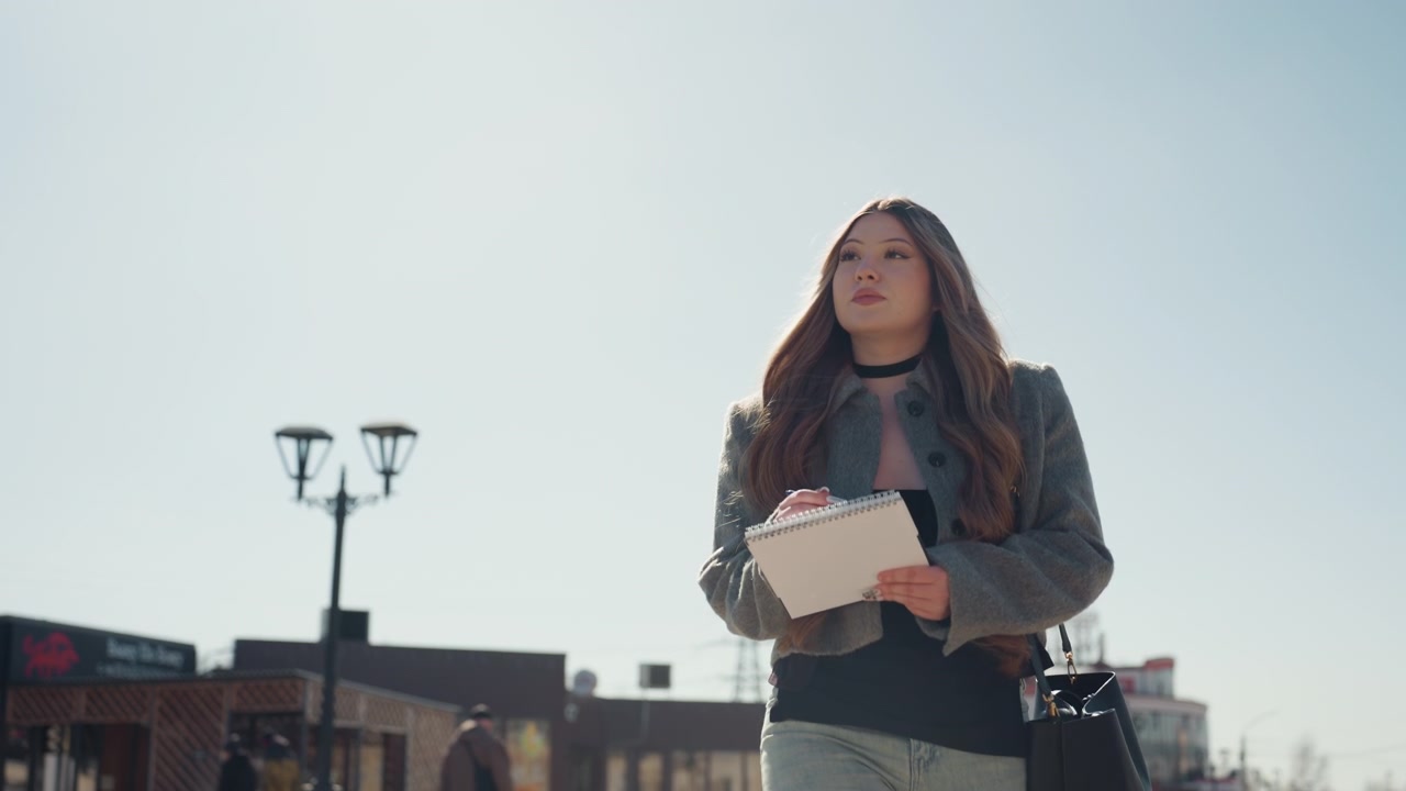 Donna casual con documenti all'esterno. Donna riflessiva che studia una lista in una piazza cittadina in un ambiente diurno. Individuo femminile profondamente concentrato sulla lettura e la presa di appunti in un contesto urbano soleggiato all'aperto.