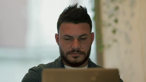 Focused-bearded-man-using-laptop-in-coffee-shop