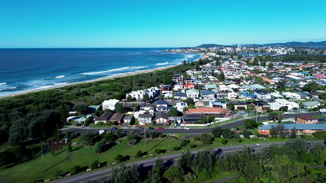 Drone aerial landscape of urban town suburbs with ocean waves crashing on shoreline and housing homes on street with road highway North Entrance Central Coast Australia community urban infrastructure