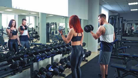 active couple lifting dumbbells together in gym. muscular man and woman holding dumbbells in their hands and doing workout while standing in front of the mirror indoors.