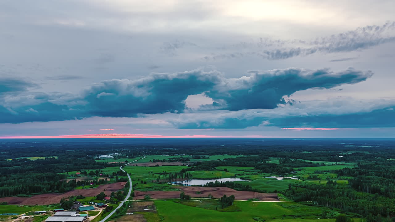 Drone hyperlapse of sunset over expansive rural farmland with winding road and green fields