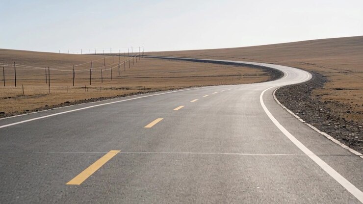 Telecamera in movimento che avanza lungo una strada a due corsie che curva a destra per rivelare un'altura, con linee tratteggiate gialle.