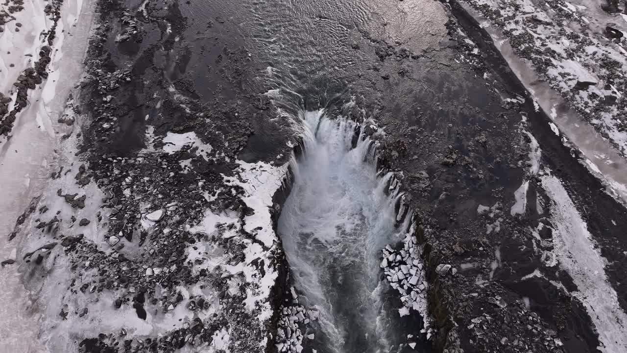 Top-down drone view of Selfoss waterfall cutting through snowy terrain in Iceland.