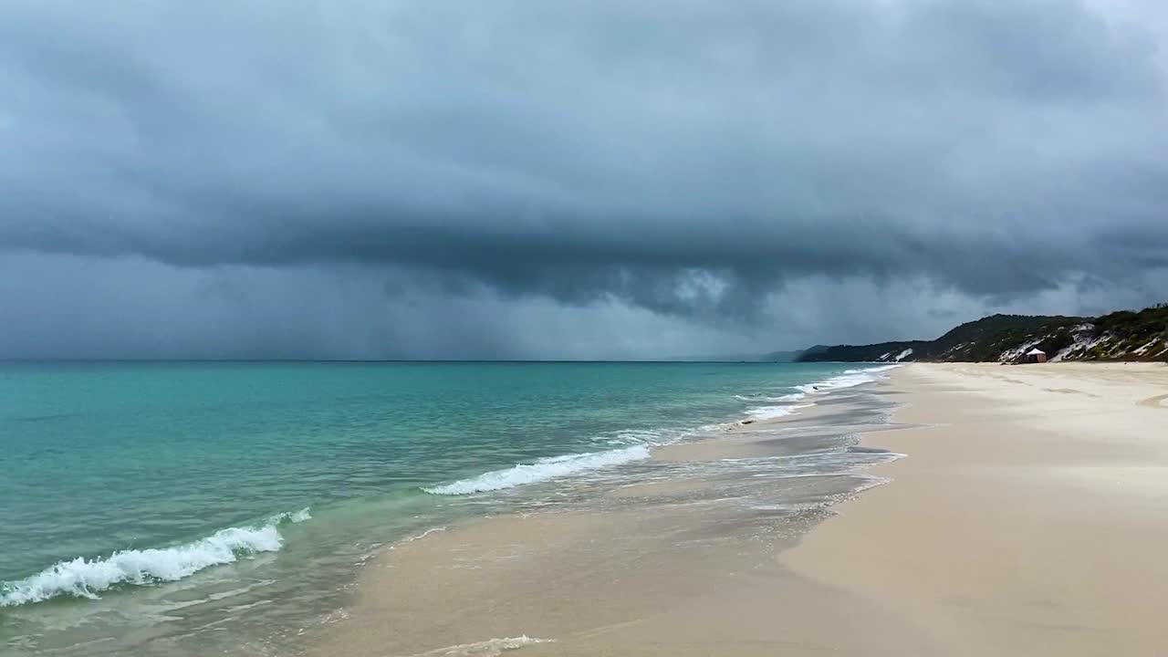 레이어와 대조 - 어둡고 성난 폭풍우가 녹색 태평양 위로 비가 내리면서 잔잔한 래핑 파도가 평화로운 해변으로 밀려옵니다.