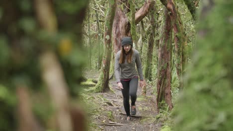 young caucasian woman with a black beanie walking up a track in a forest with moss covered trees in egmont national park, new zealand.