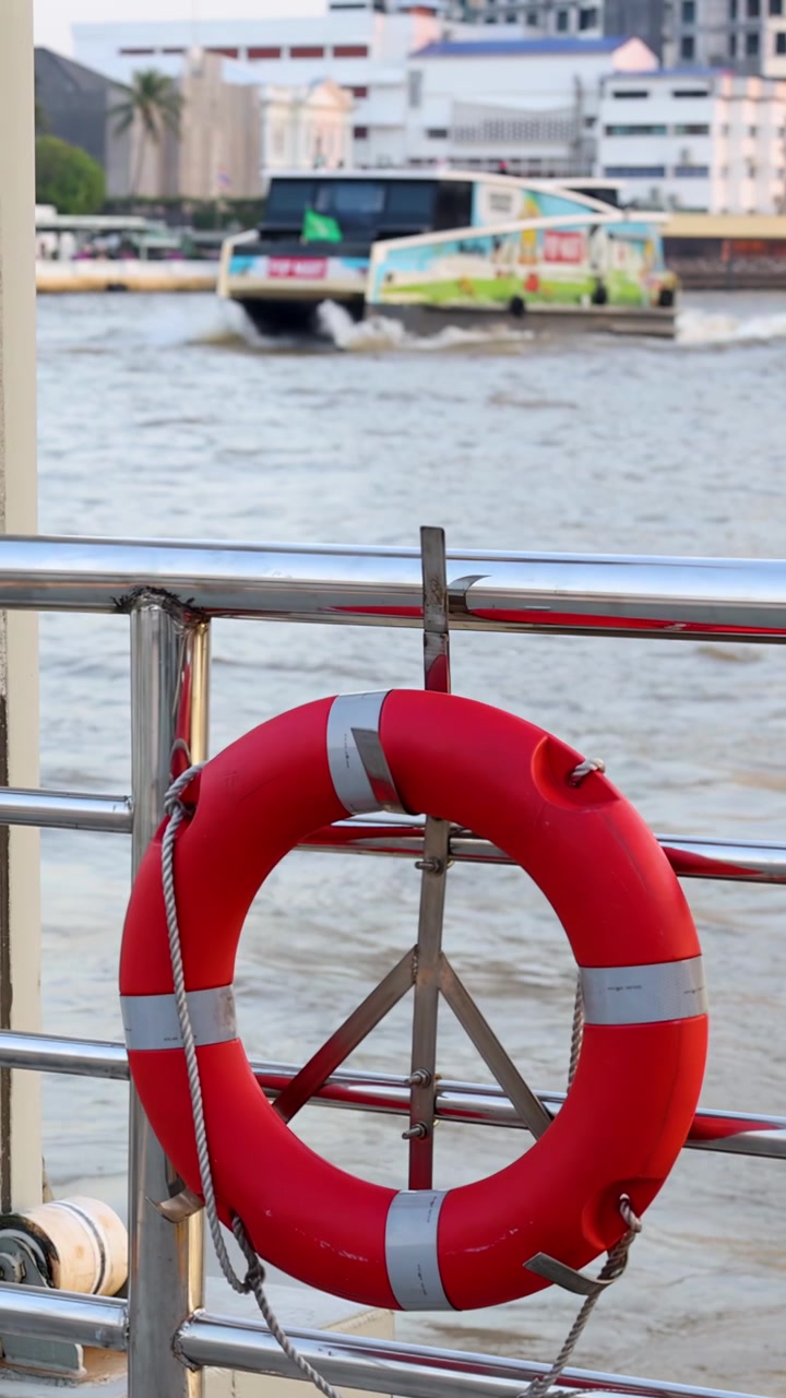 Salvagente statico sulla ringhiera del molo mentre un battello passeggeri scivola lungo un corso d'acqua fluviale urbano
