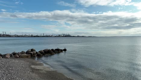 aarhus port and container terminal seen in background from marselisborg beach in aarhus denmark - forward moving aerial close to ground and sea