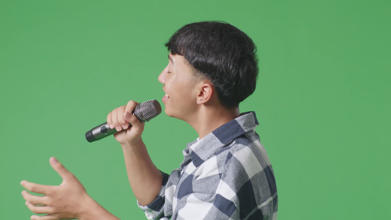 녹색 스크린 배경에서 마이크를 들고 노래하는 젊은 아시아 십대 소년의 가까운 측면 시각