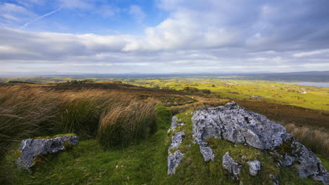 timelapse of rural nature farmland with grass field rocks in the foreground and sheep and lake in distance during sunny cloudy day viewed from carrowkeel in county sligo in ireland