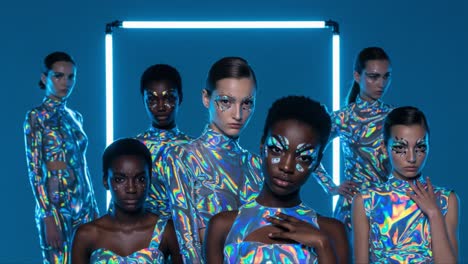 a captivating display of futuristic fashion: a group of models in iridescent outfits with stunning makeup posing against a neon-illuminated backdrop