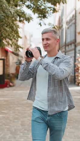 happy mature caucasian man making photo pictures on camera looking around while walking in city