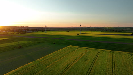 Amplios-Campos-Verdes-Con-Turbinas-Eólicas-Al-Atardecer,-Pueblo-Lejano,-Luz-Dorada,-Vista-Panorámica