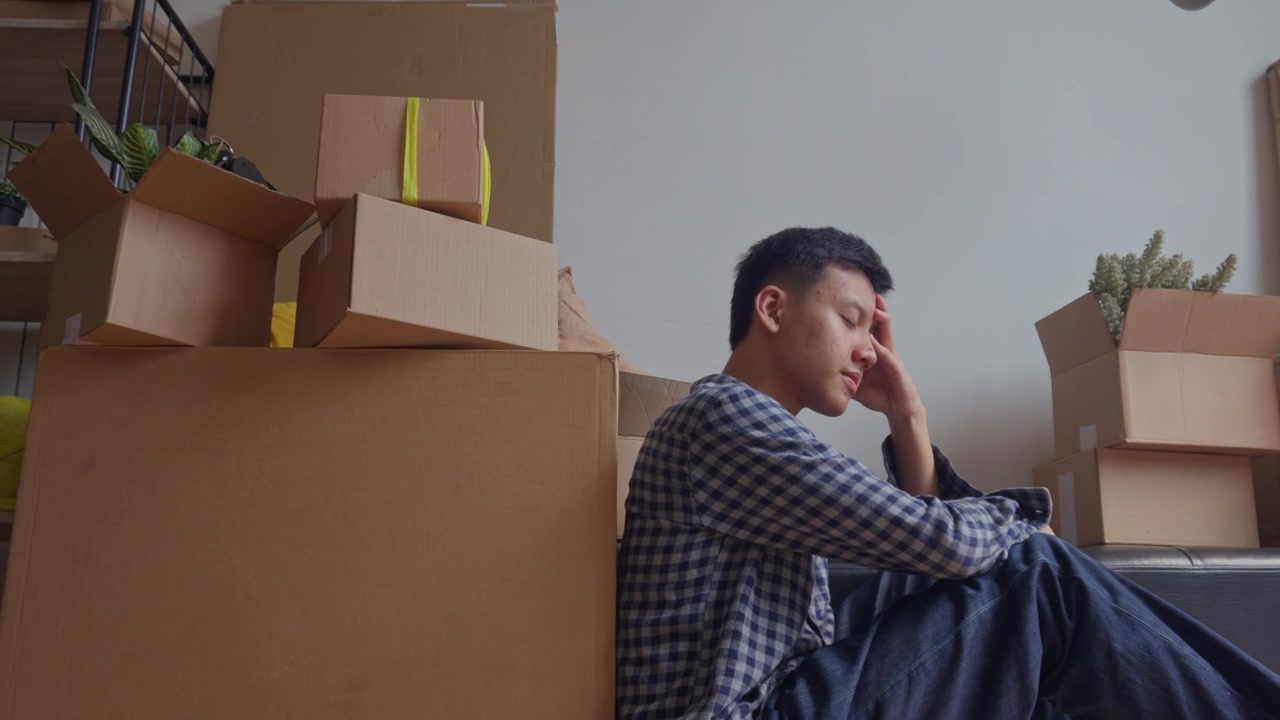 Exhausted and overwhelmed man sits on floor amidst packed cardboard boxes