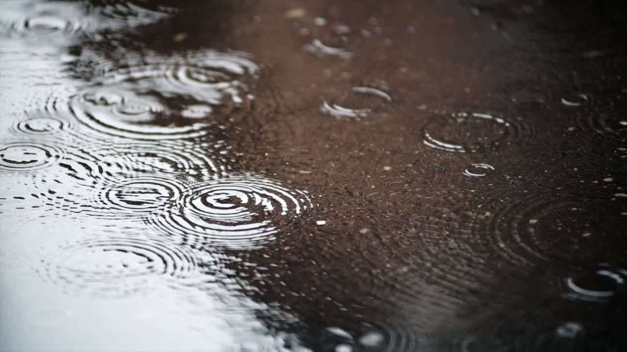 RAINWATER DROPS FALLING ON A PUDDLE WITH REFLECTS IN A STREET