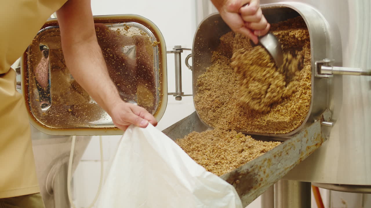 Craft beer production factory, brewery manufacture. Man trying beer in glass close-up. Brewer portrait, cooking alcohol in metal vats bottles