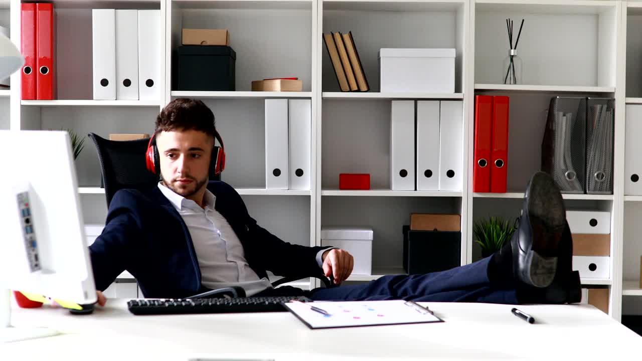 헤드폰을 착용 한 사업가 가 테이블 에 다리를 놓고 일 하고 있다