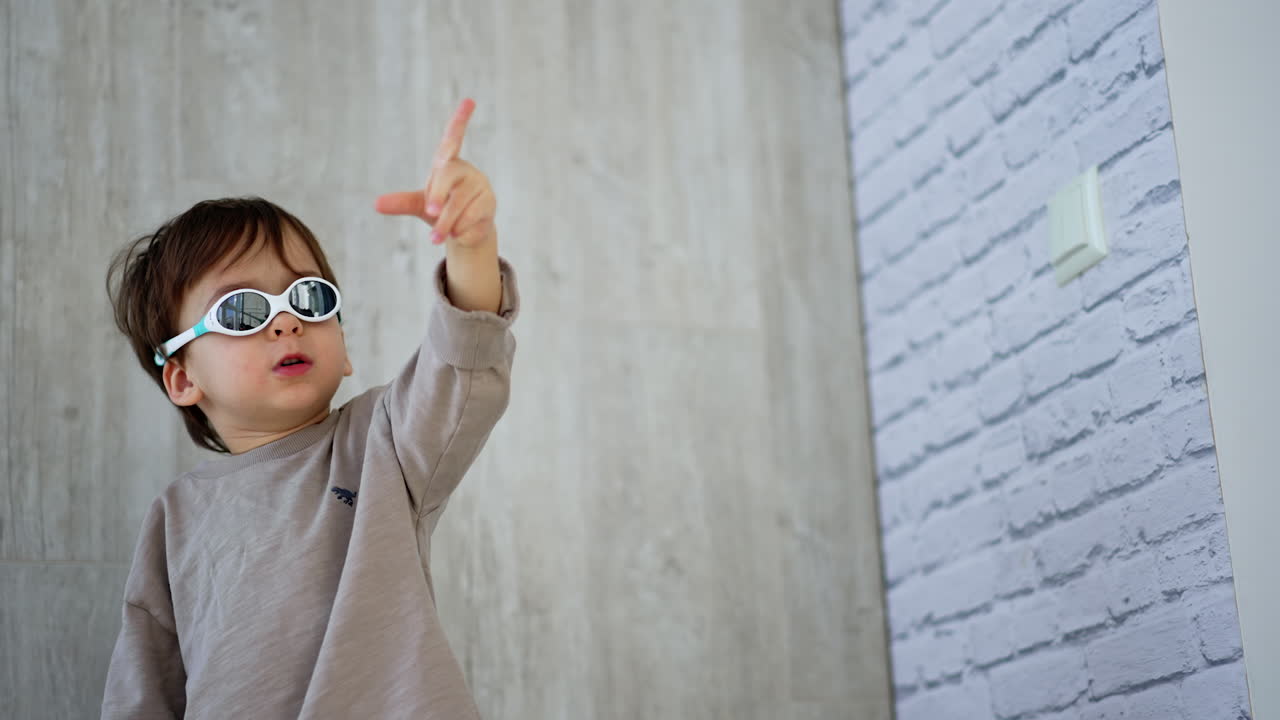 Caucasian kid in sunglasses switches on the light. Adorable baby boy points up with his finger. Low angle view.