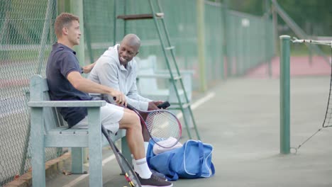 amigos varones felices diversos sentados en el banco hablando en la cancha de tenis, cámara lenta
