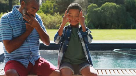 Grandson-and-grandfather-making-funny-faces-near-poolside