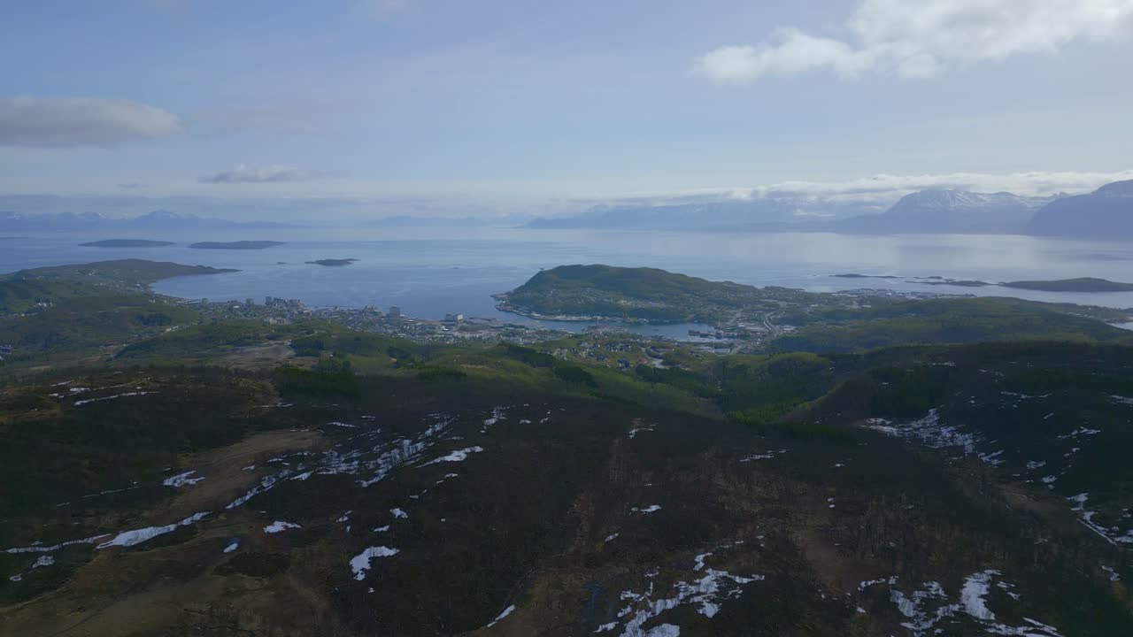 A coastal town with a TV tower on a hill, surrounded by islands and mountains under a clear sky.