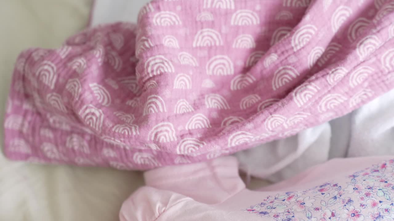 Baby's hand is holding pink bed linen close up