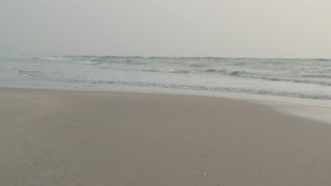 close view of sandy beach with gentle waves at dusk, hint of orange sky on horizon, calm atmosphere