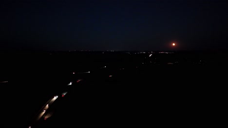 headlights and backlights of cars on highway in american town at night. aerial wide shot. lighting full moon at blue dark sky at nightscape. busy traffic in suburbia of usa