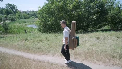 young man walking with guitar on street near forest