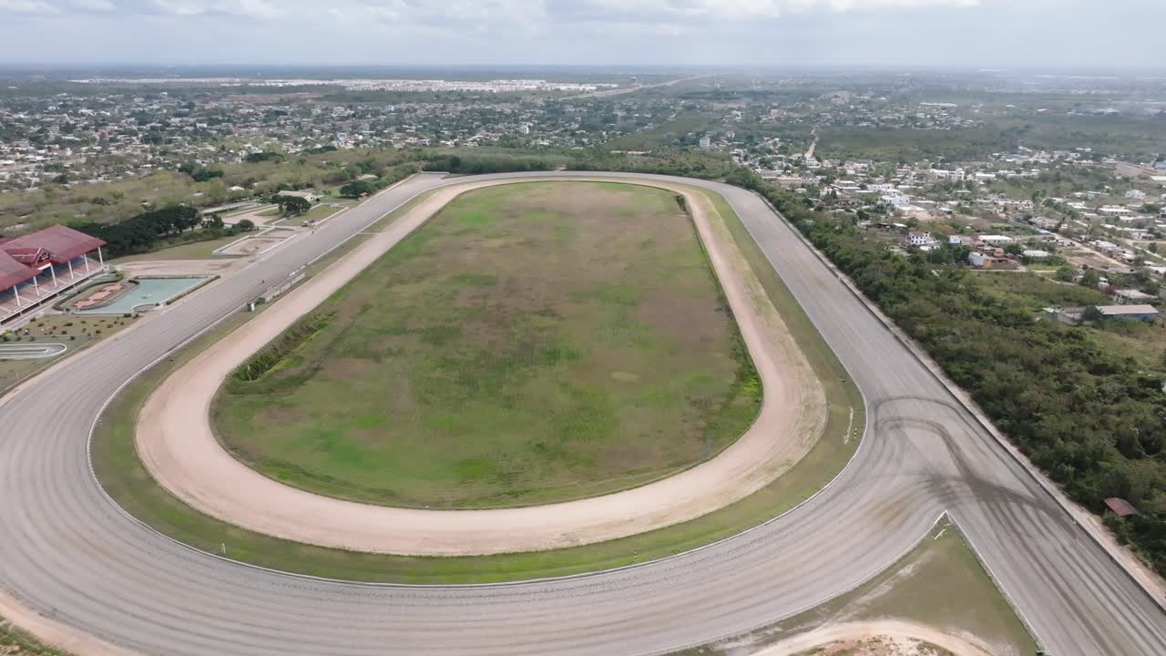 toma aérea de arriba hacia abajo del hipódromo vacío en una zona rural con la ciudad en el fondo, república dominicana