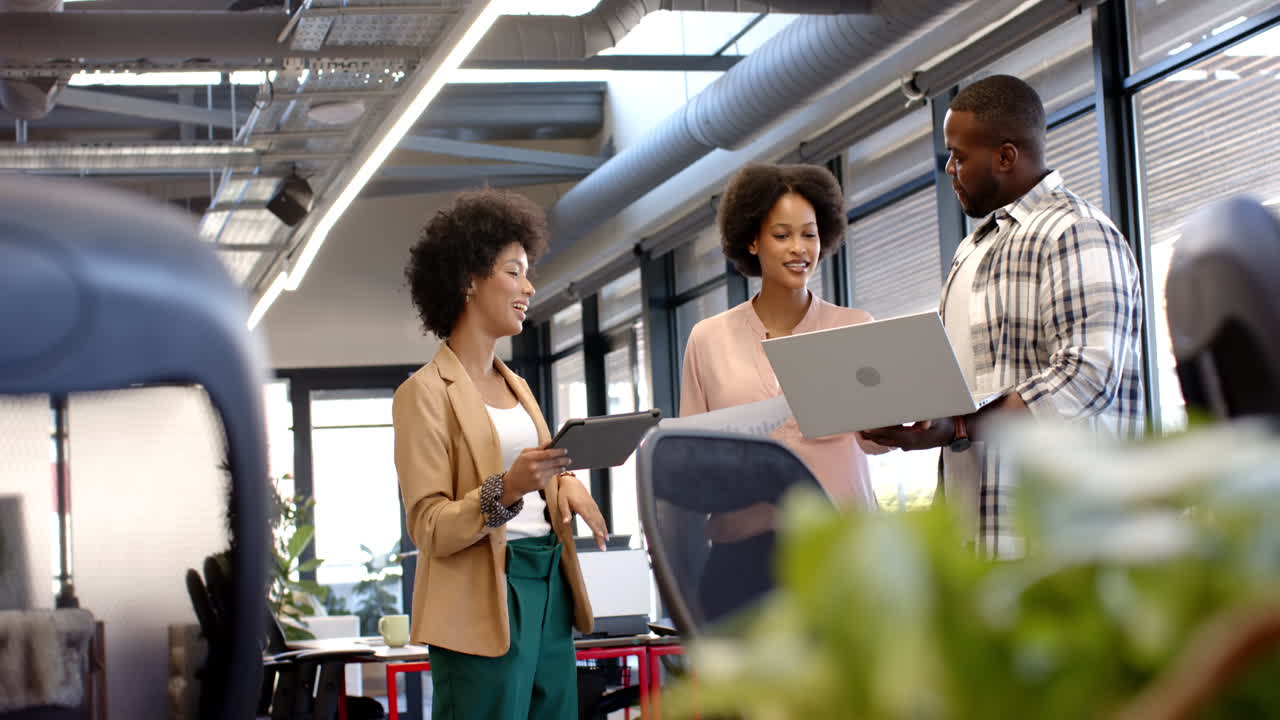 Professionals discussing work while holding laptop and tablet in office