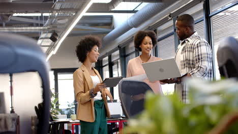 professionals discussing work while holding laptop and tablet in office