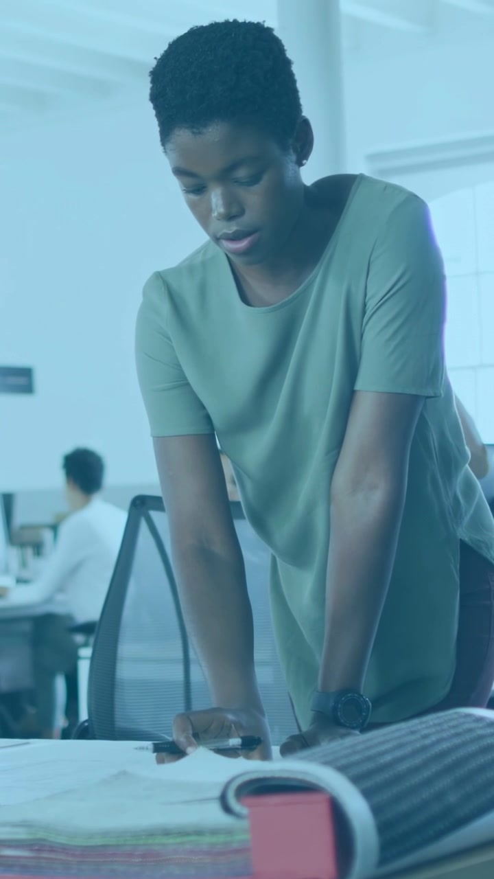 Vertical video: Designer leaning on table, marking papers, sparking code overlays for design review