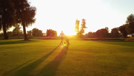 disparo de un dron de ángulo bajo después de que un golfista caminara con un carrito en un campo de golf durante una increíble puesta de sol