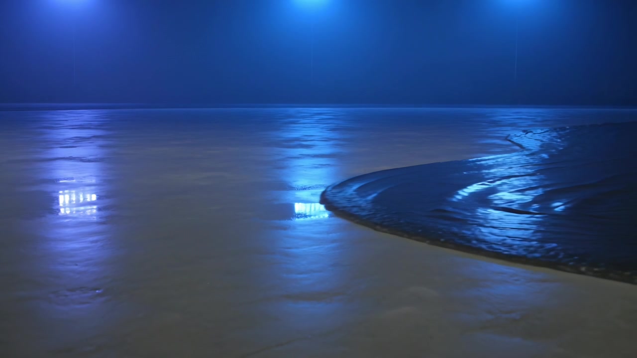 Eintreffende Welle schiebt gekrümmte nasse Uferlinie nachts über Sand und bildet Wellen unter 3 blauen Lichtern.