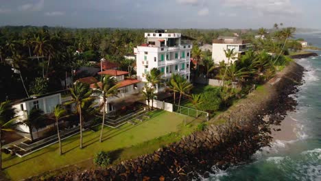 aerial footage of a hotel along the coast of ahangama, sri lanka, showing a lush landscape with palm trees and ocean waves hitting the rocky shoreline.