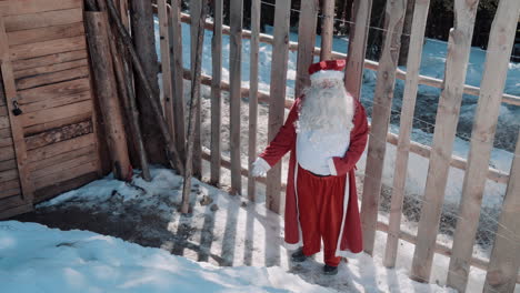 santa walks along a snowy path to a wooden house with a wooden fence