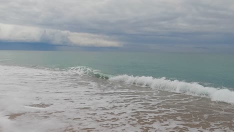 ola de mar de playa de arena gruesa en cámara lenta a 120fps 4k día nublado agua turquesa olas de mar individuales gran playa vacía