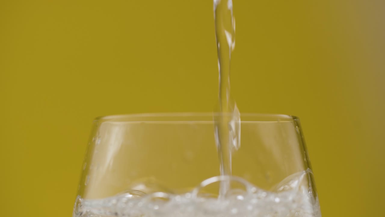 Vista laterale di acqua frizzante che riempie un bicchiere, sfondo giallo isolato