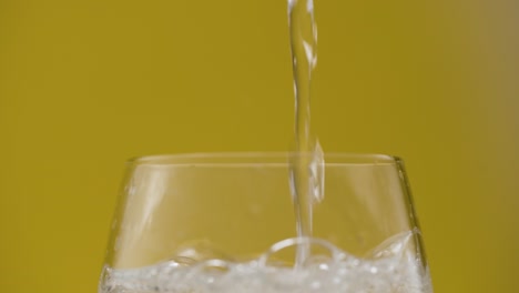 seitenansicht mit sprudelndem wasser, das ein glas füllt, isolierter gelber hintergrund