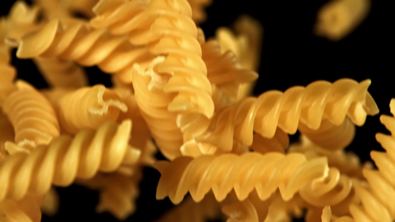 Fusilli che cadono al rallentatore su sfondo nero.