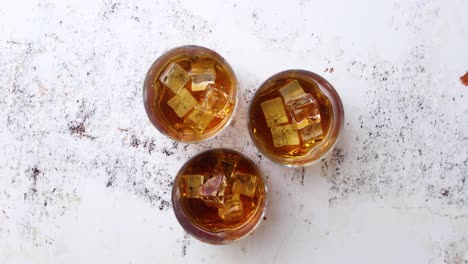 three glasses of whisky and ice rotating on speckled table