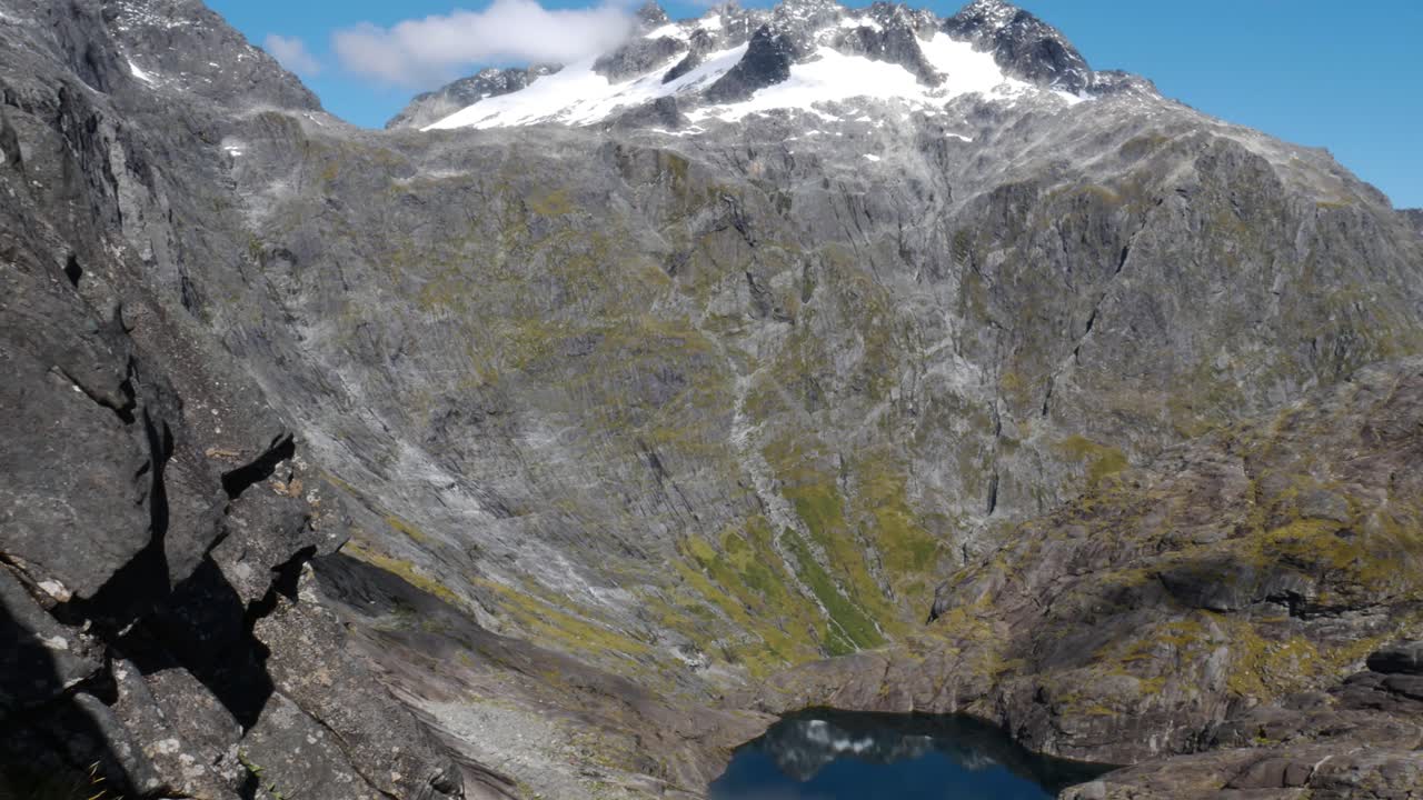 Panning shot of giant mountain range and natural hidden lake in the valley during Gertrude Saddle Hike in Summer,NZ