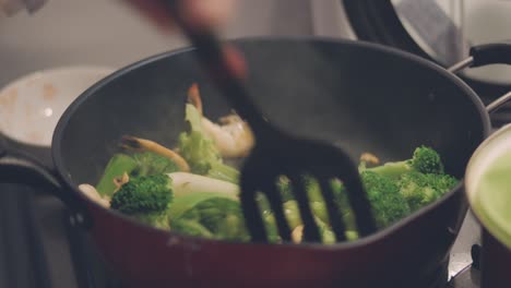 cooking and pouring soy sauce into the stir-fried brocolli with prawns on the frying pan