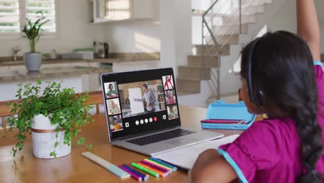 Schoolgirl-using-laptop-for-online-lesson-at-home,-with-diverse-teacher-and-class-on-screen