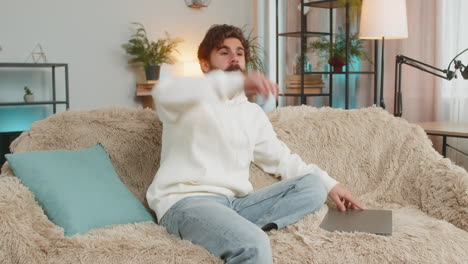 happy indian man sitting on couch closing laptop and relaxing after finishing work in living room