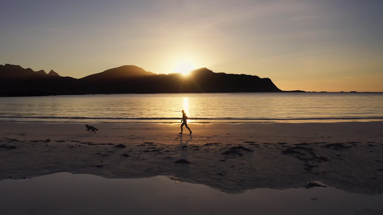 fotografía lateral de una corredora corriendo en una playa con su perro golden retriever al atardecer, islas lofoten, noruega