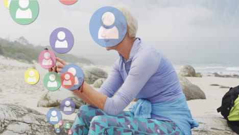 animation of digital people icons over senior woman by seaside using smartphone