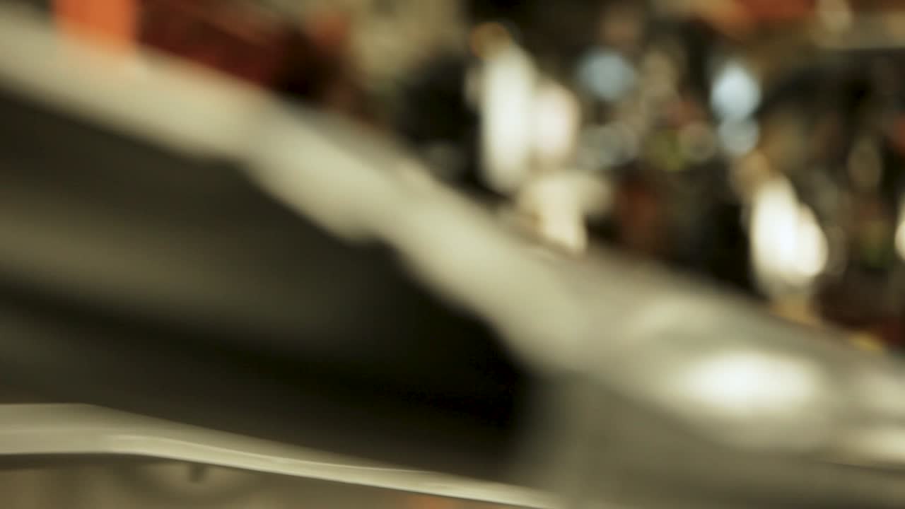 attraverso una telecamera statica, un braccio robotico nero con una pinza d'argento presenta un telaio bianco della porta dell'auto, con un buco rettangolare centrale, tutto all'interno di un ambiente di fabbrica sfocato sullo sfondo