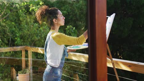 Mixed-race-woman-painting-on-canvas-in-the-balcony-at-home