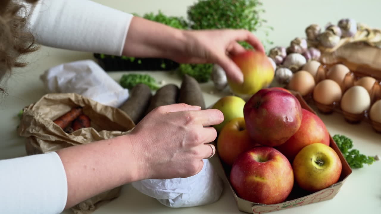 Woman arranging apples near groceries in sustainable packaging on a table